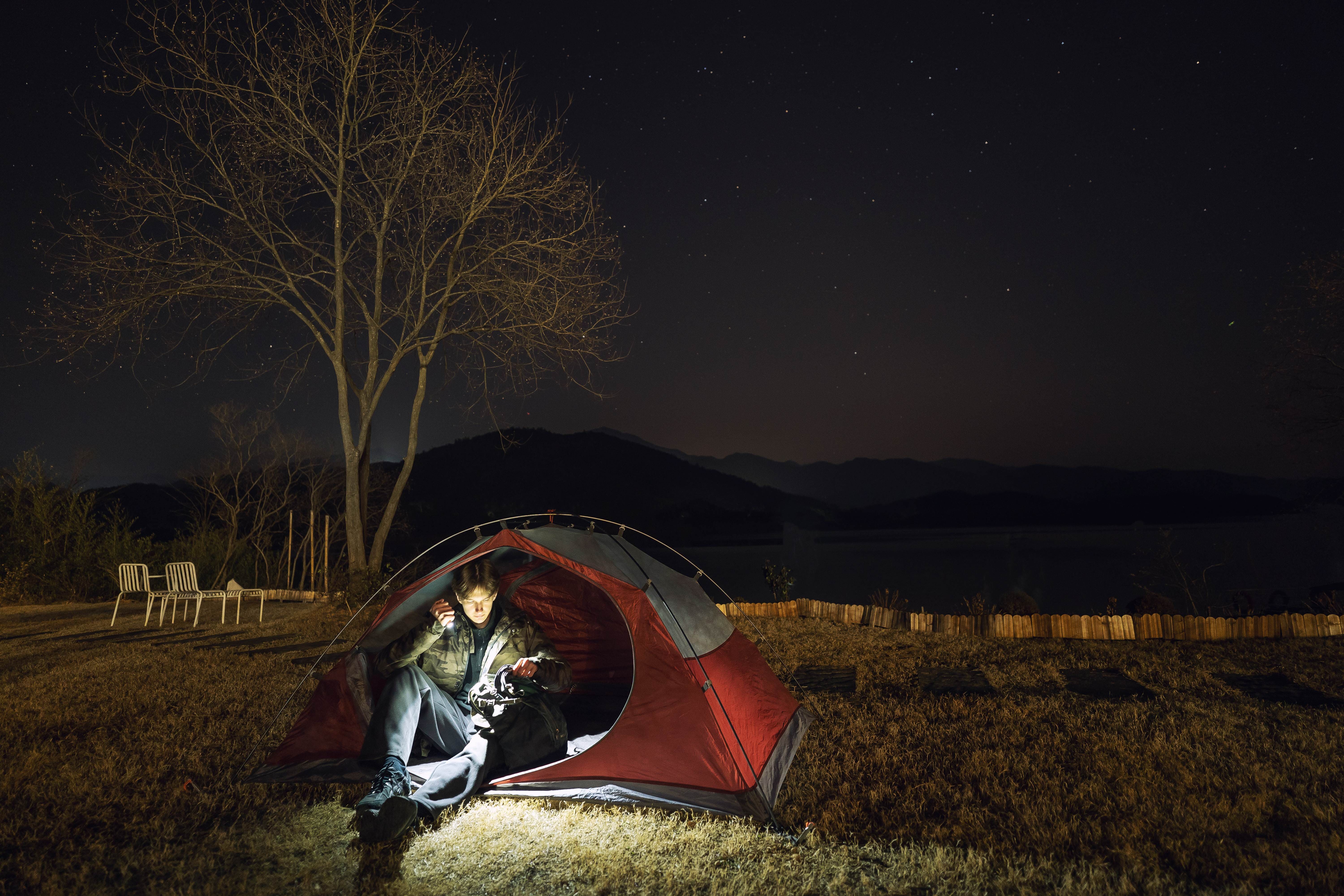 Man using a flashlight inside a red tent