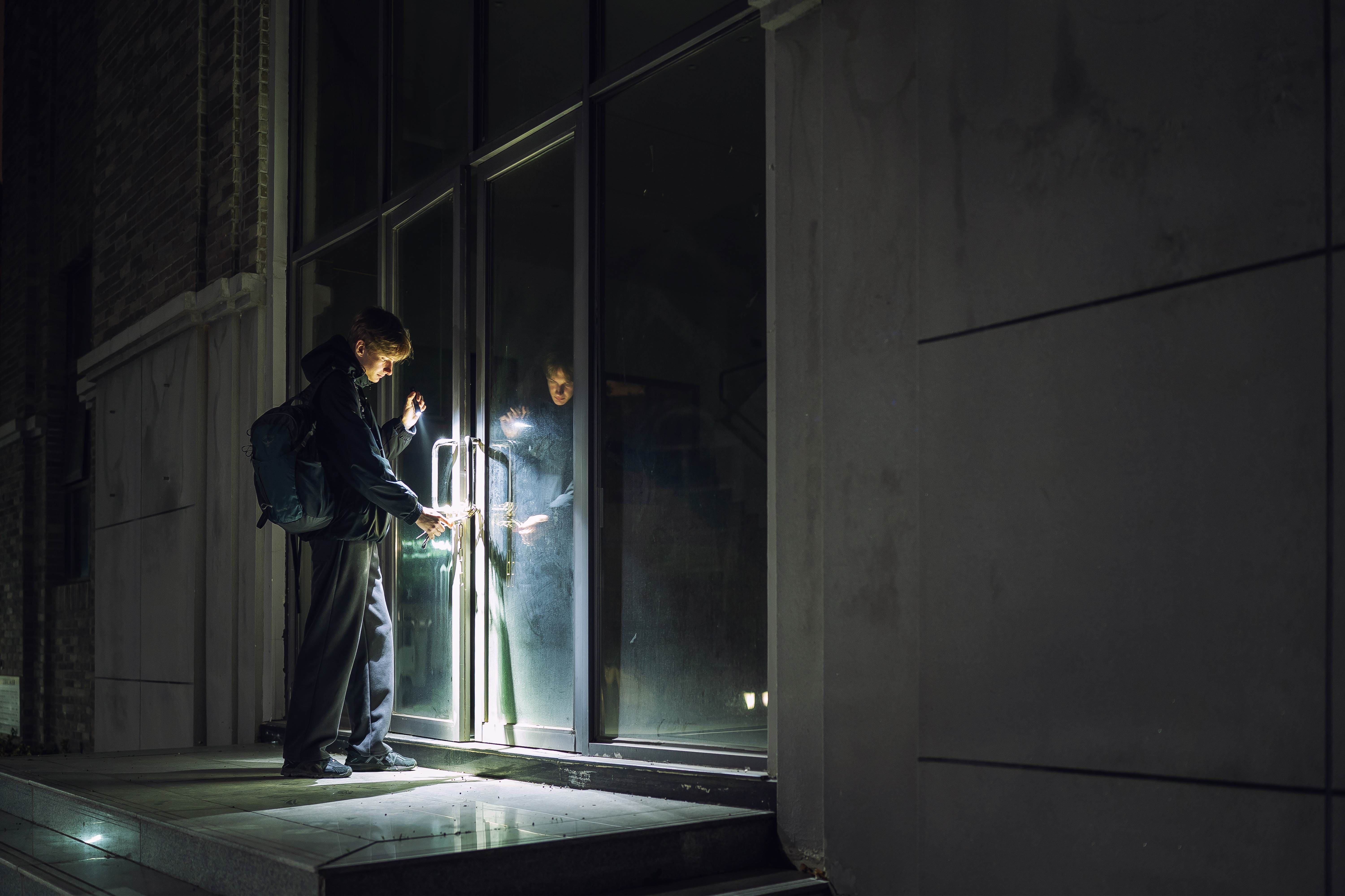 Tentative d'effraction nocturne d'un cambrioleur utilisant une lampe torche pour forcer la serrure d'une porte vitrée.