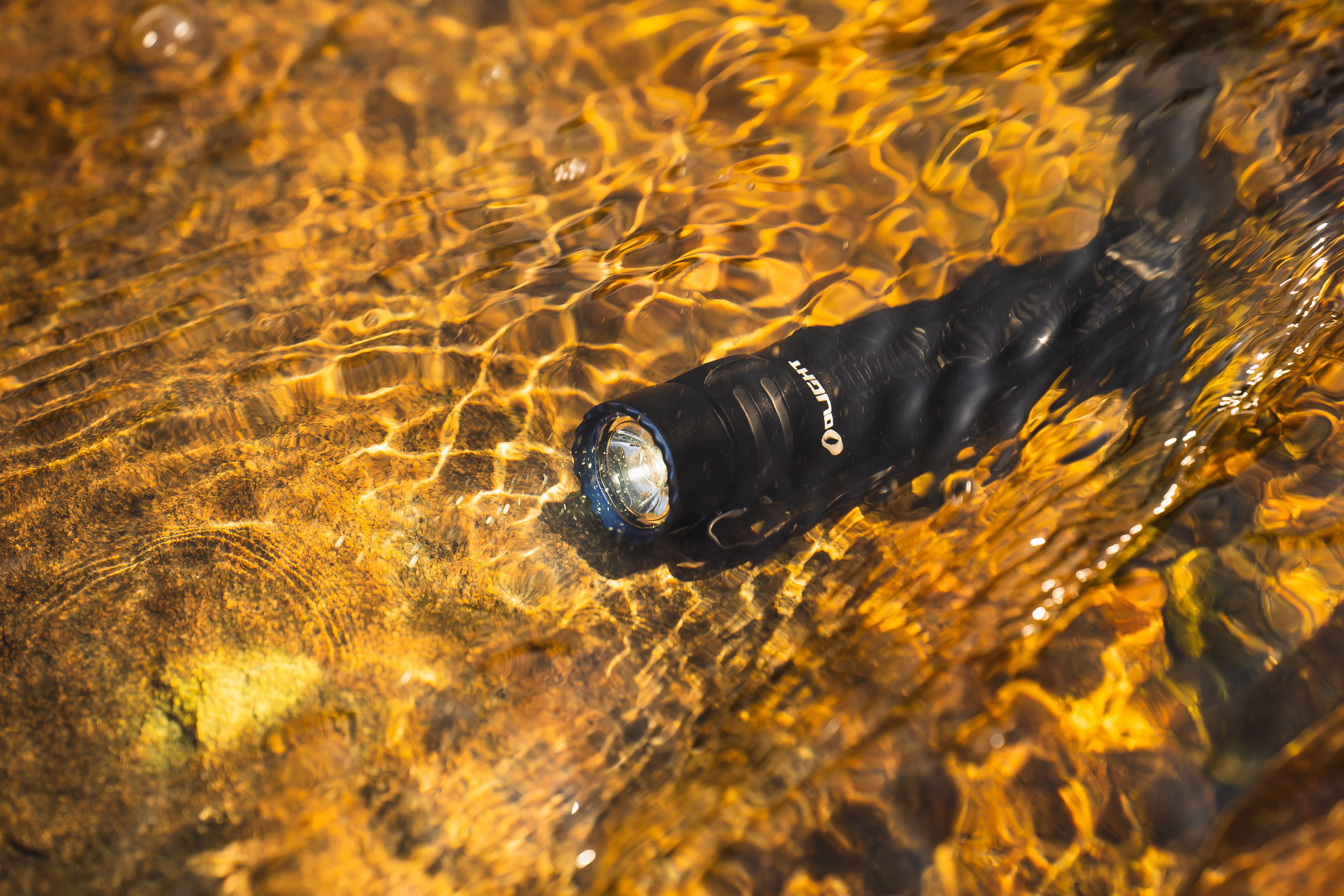 水中に沈むOlight懐中電灯、水面からの光が反射する様子。