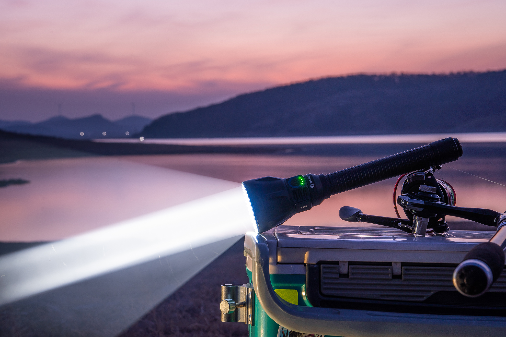 Powerful flashlight illuminating a lake at dusk, next to fishing gear on a cooler