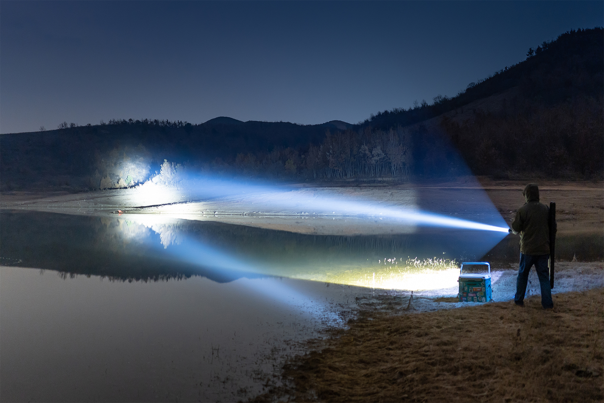 Man illuminates frozen lake and distant shore with bright flashlight