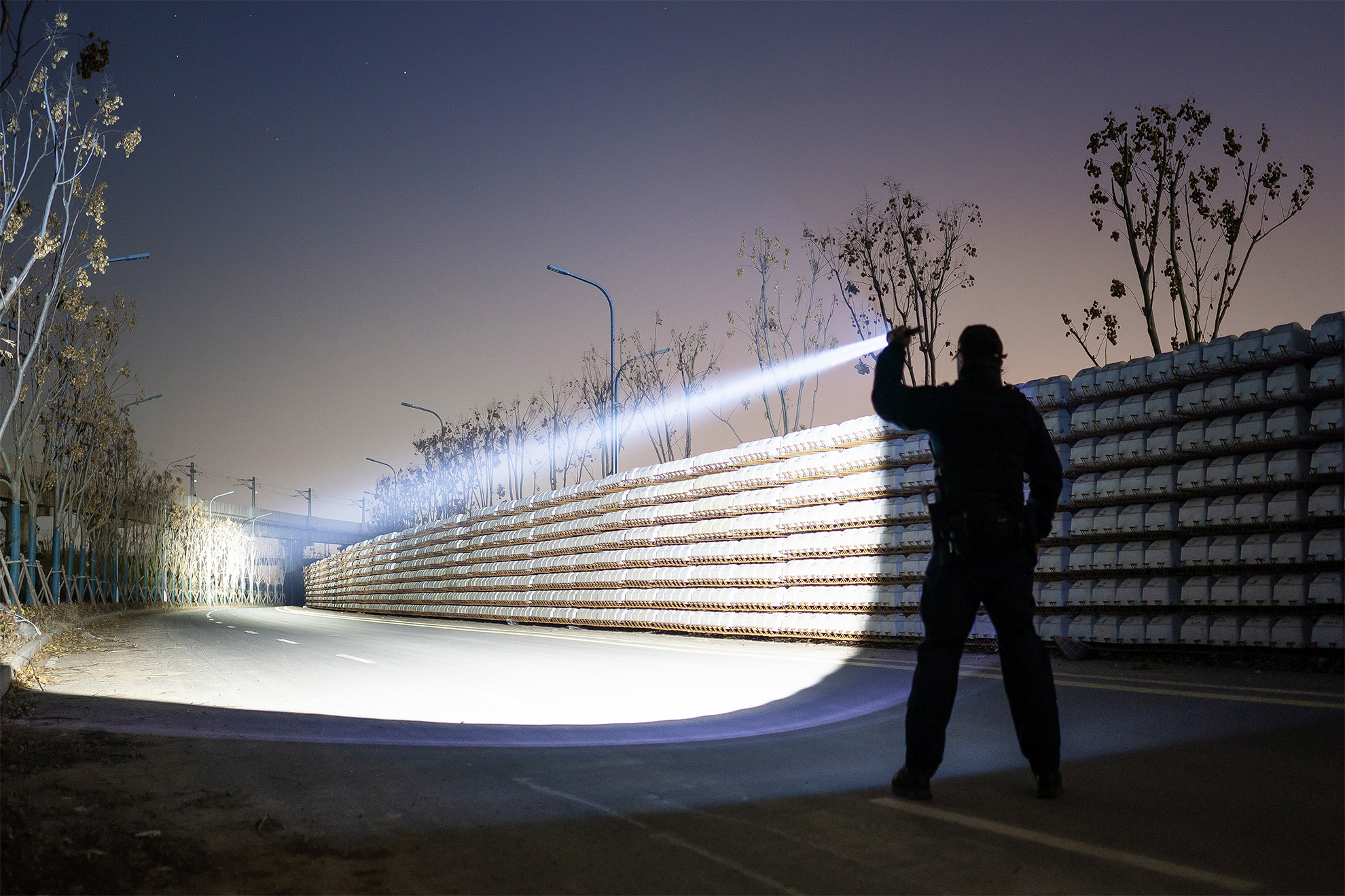 Hombre con linterna potente iluminando una carretera oscura. Haz de luz brillante destacando la visión nocturna a lo largo de una barrera.