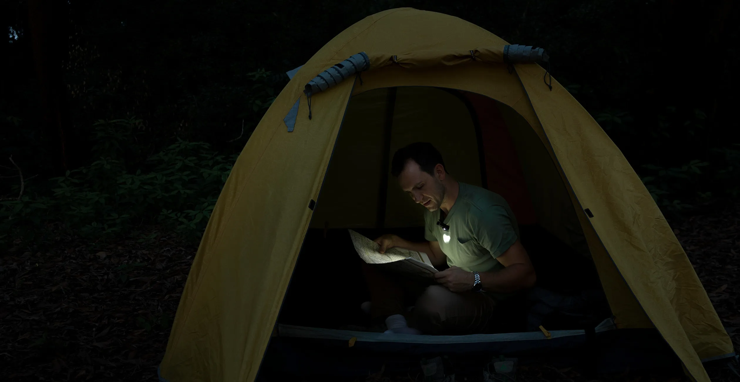 Camper examining track maps inside tent using regulated head torch beam