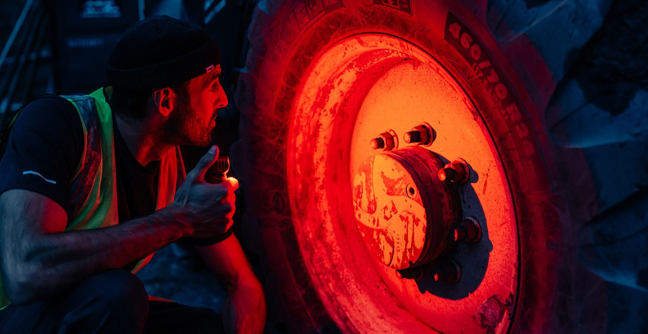 Mechanic inspecting large tractor tire with red light illumination during night maintenance