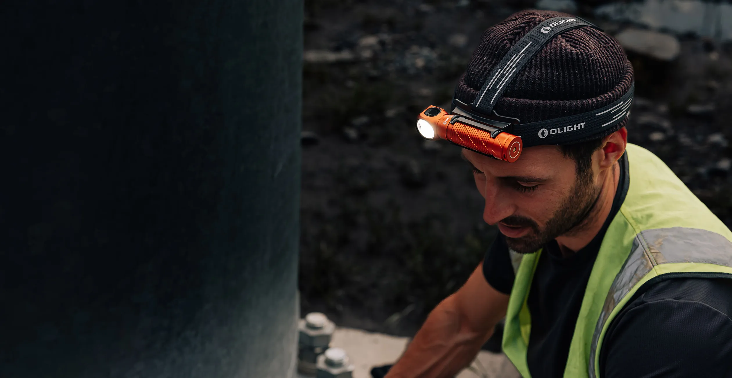 Worker wearing an Olight LED rechargeable headlamp on a beanie for hands-free outdoor industrial maintenance work.