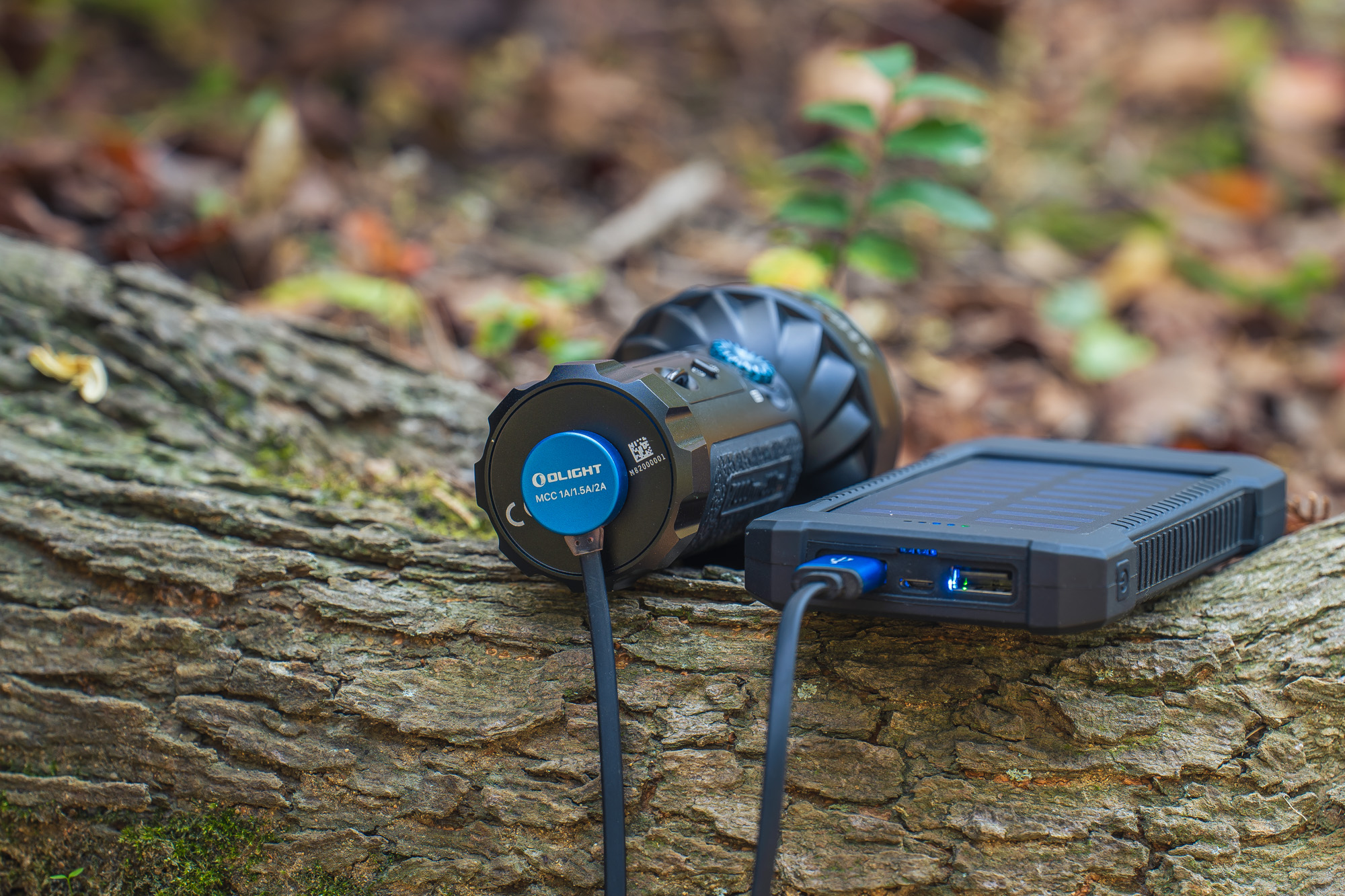 Linterna Olight cargándose con un power bank solar en un tronco de árbol.