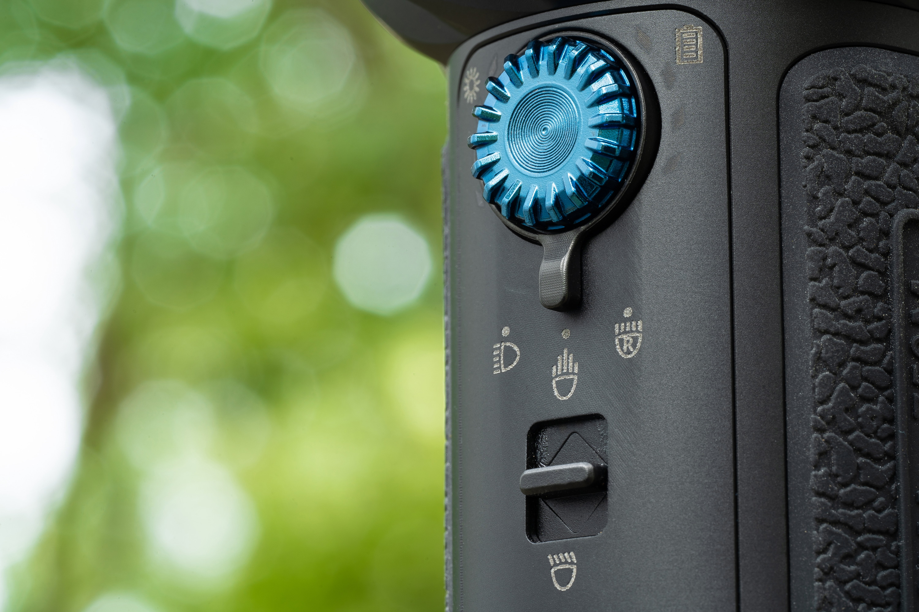 Panel de control de dispositivo con perilla azul, interruptor e iconos de luces para ajustes de iluminación.