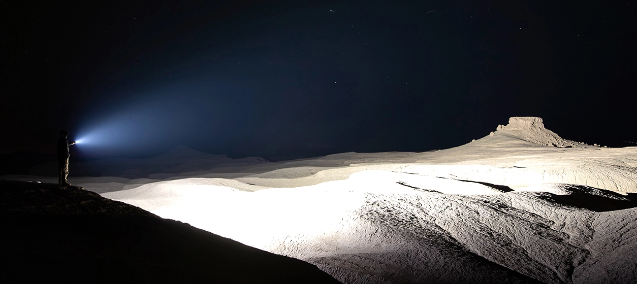 Powerful high-lumen tactical flashlight illuminating a vast desert landscape at night, showing strong beam distance and brightness.