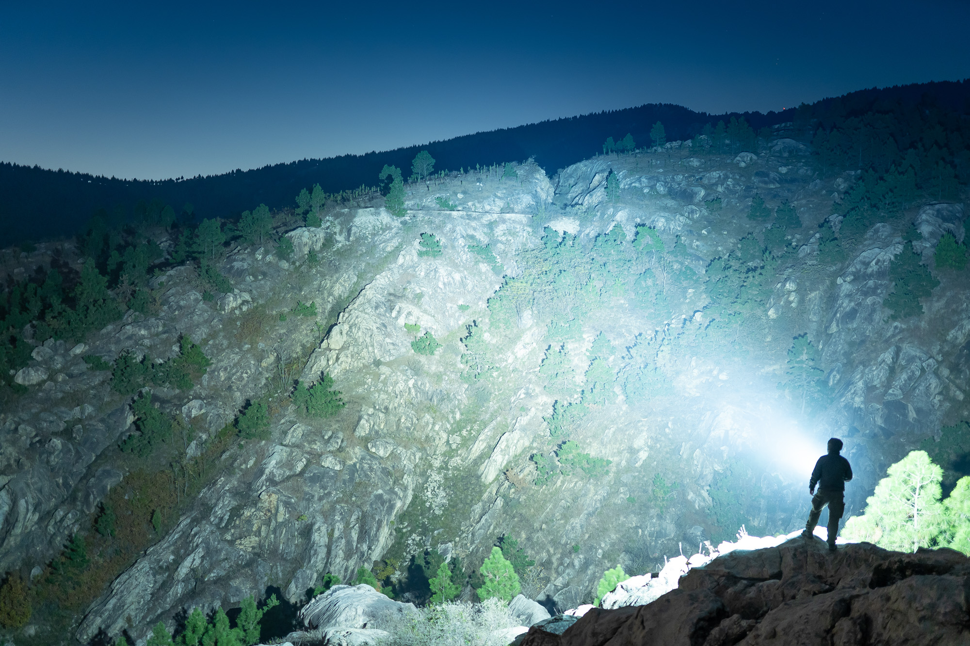 Hombre con linterna potente iluminando una montaña rocosa por la noche.