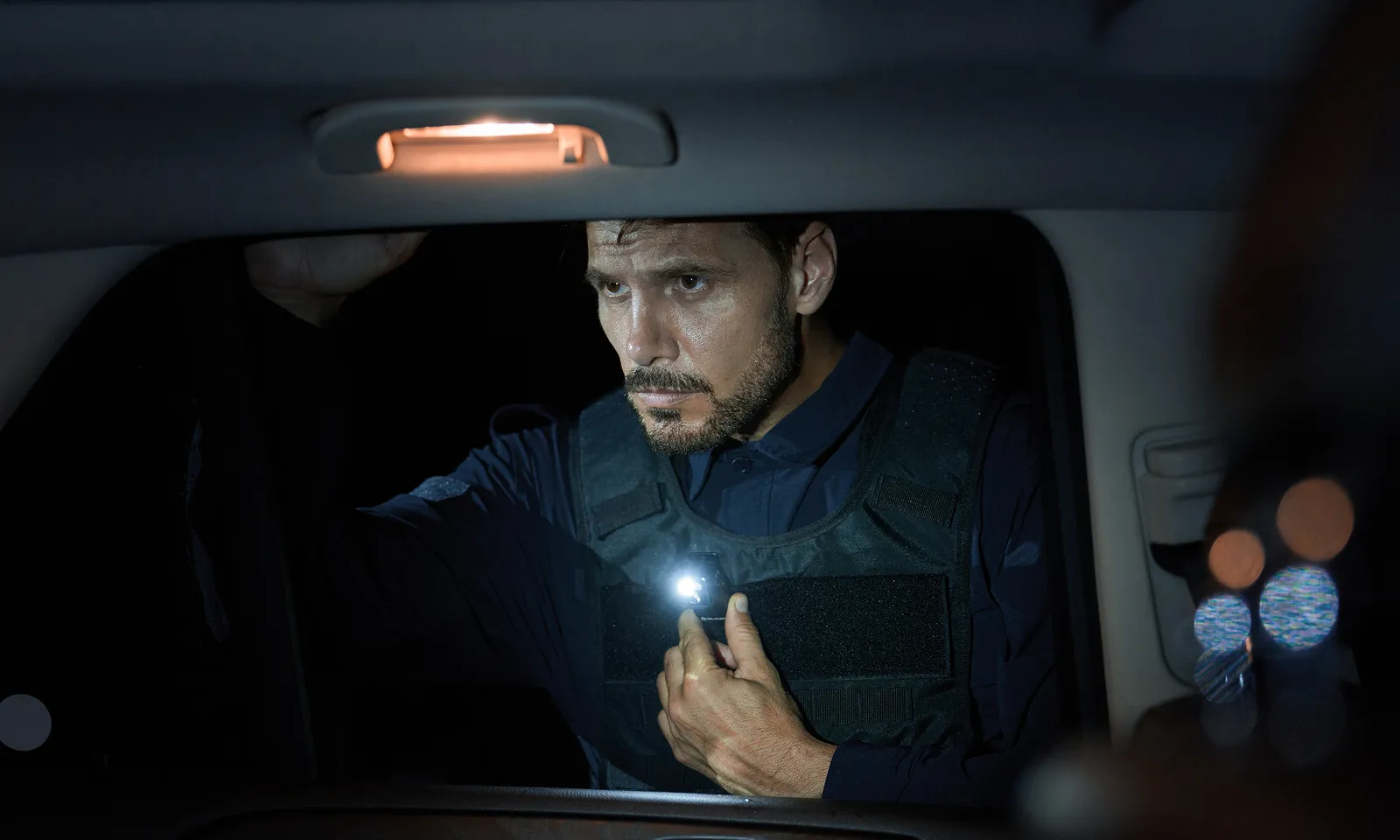 Policier en gilet tactique effectuant un contr&ocirc;le de nuit avec une petite lampe torche LED fix&eacute;e sur sa veste