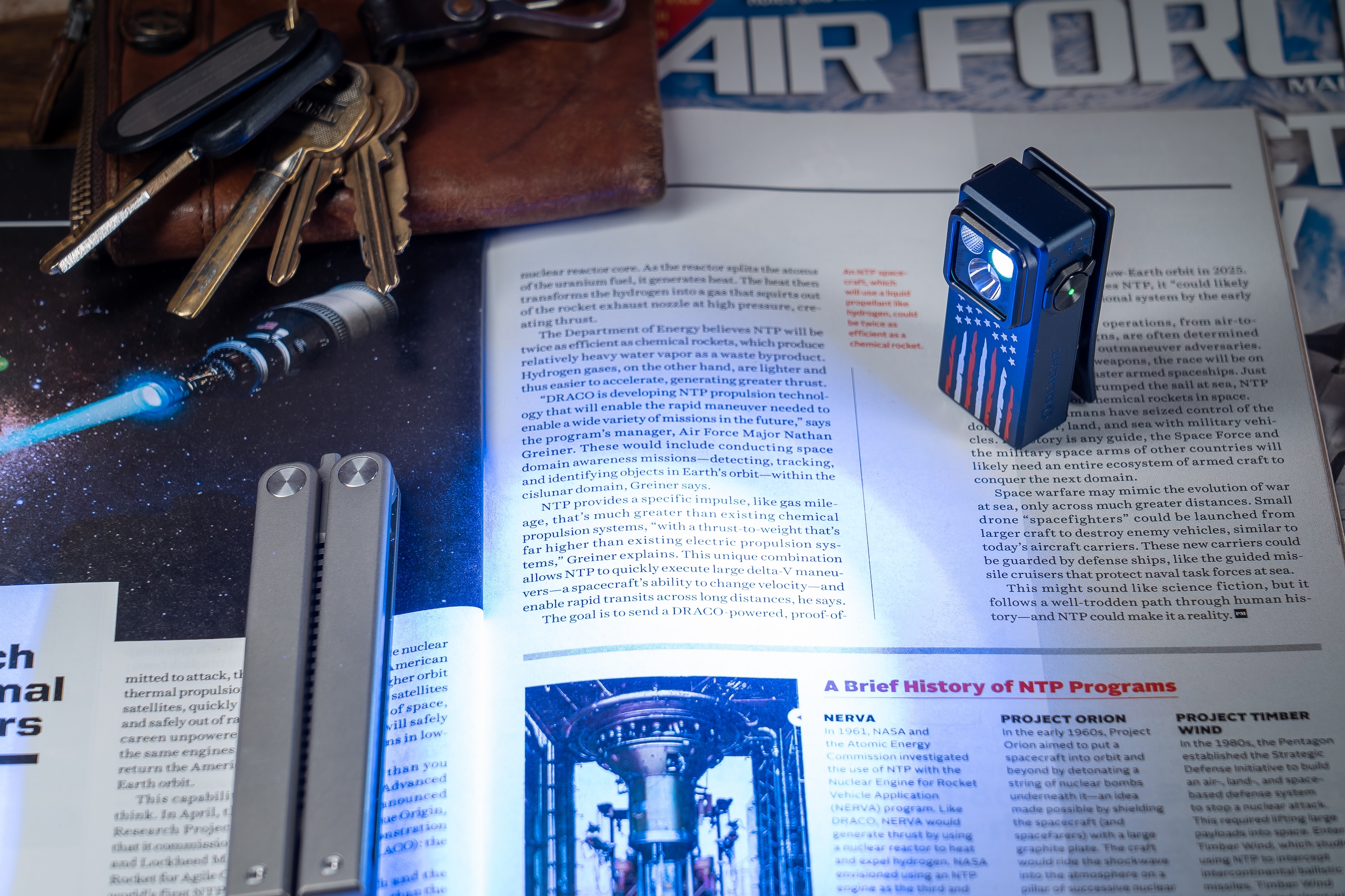 우주선 그림과 열쇠, 멀티툴이 놓인 항공우주 잡지 위 미국 국기 패턴 플래시라이트