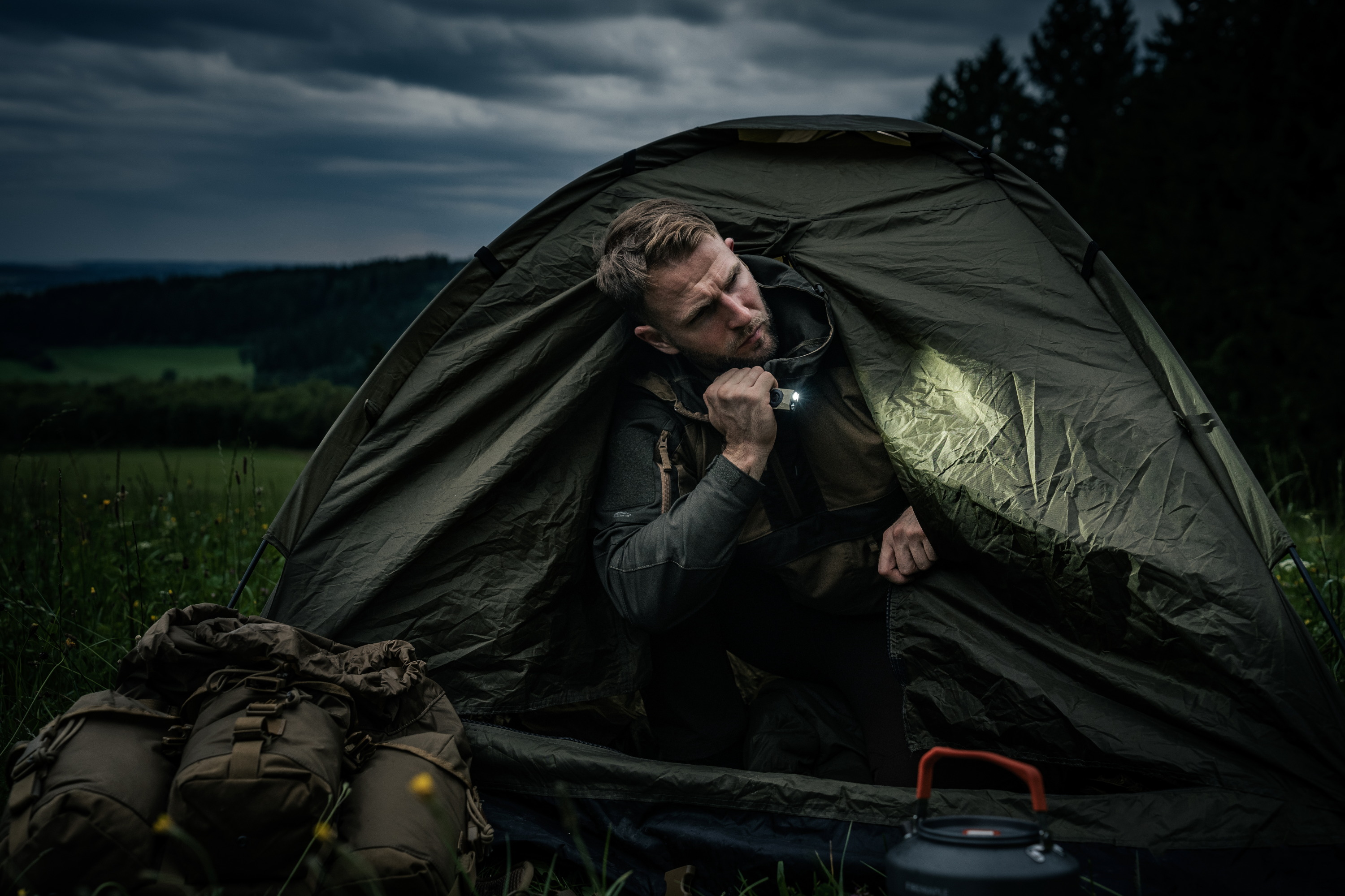Man holding bright EDC flashlight outside green camping tent