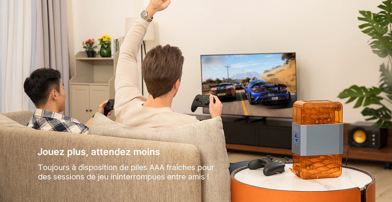 Deux amis jouent intensément aux jeux vidéo sur grand écran, l'un célébrant. Une station de piles AAA est à portée de main, garantissant des sessions ininterrompues pour un divertissement maximal.