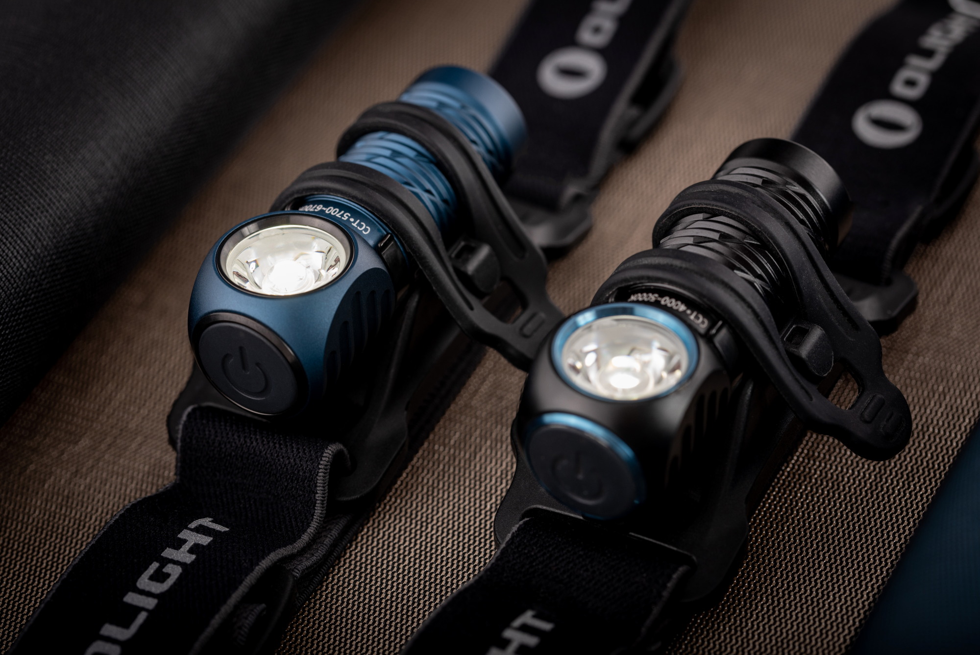 Two Olight rechargeable headlamps, one blue and one black, mounted on their elastic headbands for camping and hiking.