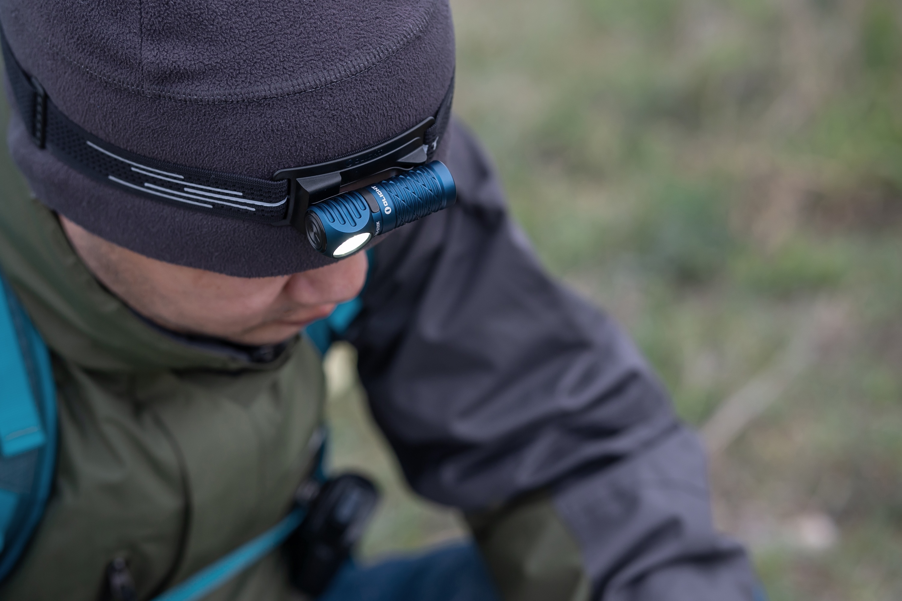 Olightの青いヘッドランプを着用し、夜間ハイキングやキャンプを楽しむ男性。