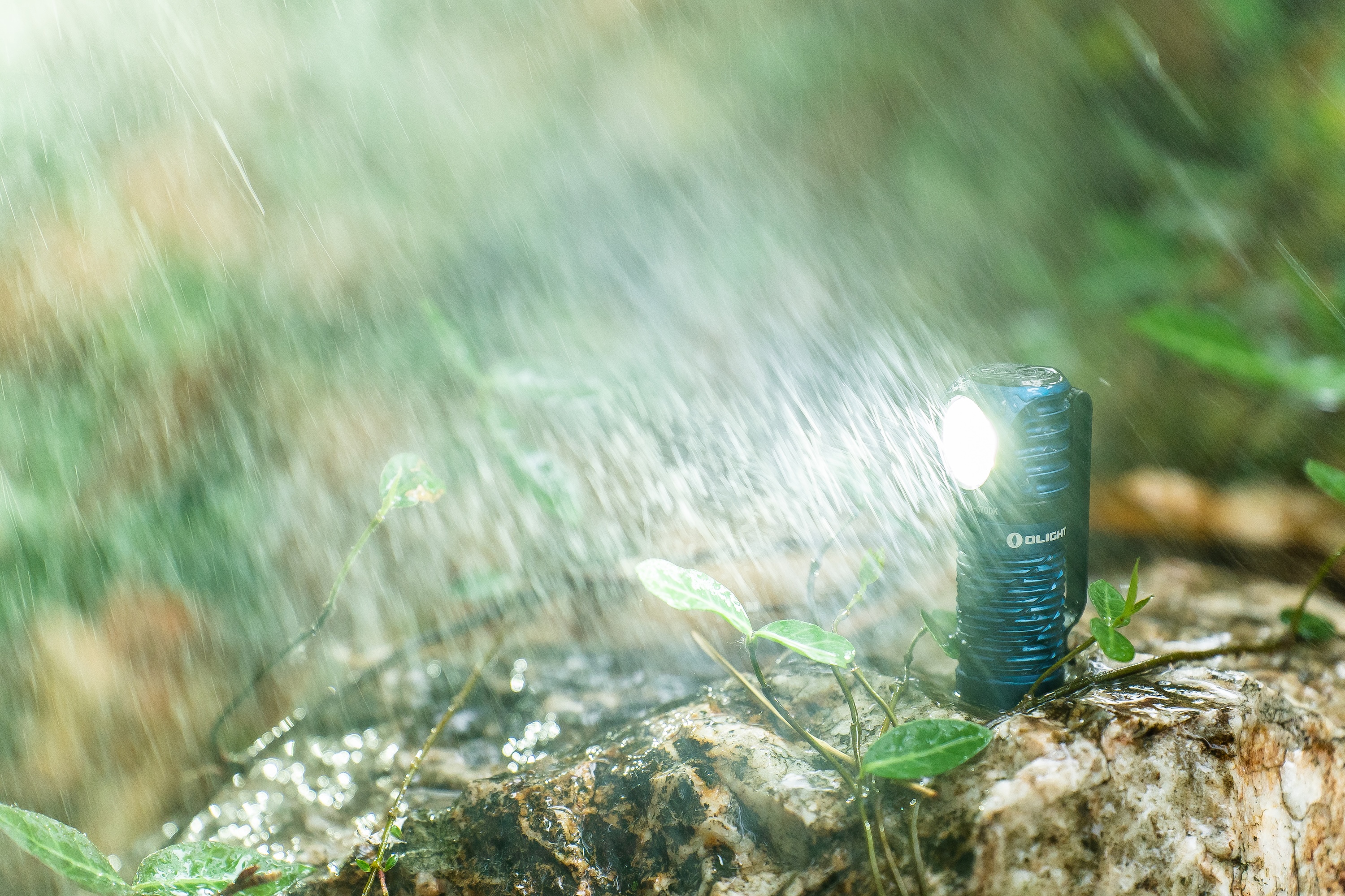 雨降る屋外の岩の上で、Olightの懐中電灯が明るく周囲を照らす。高い防水性を示すアウトドア用品。