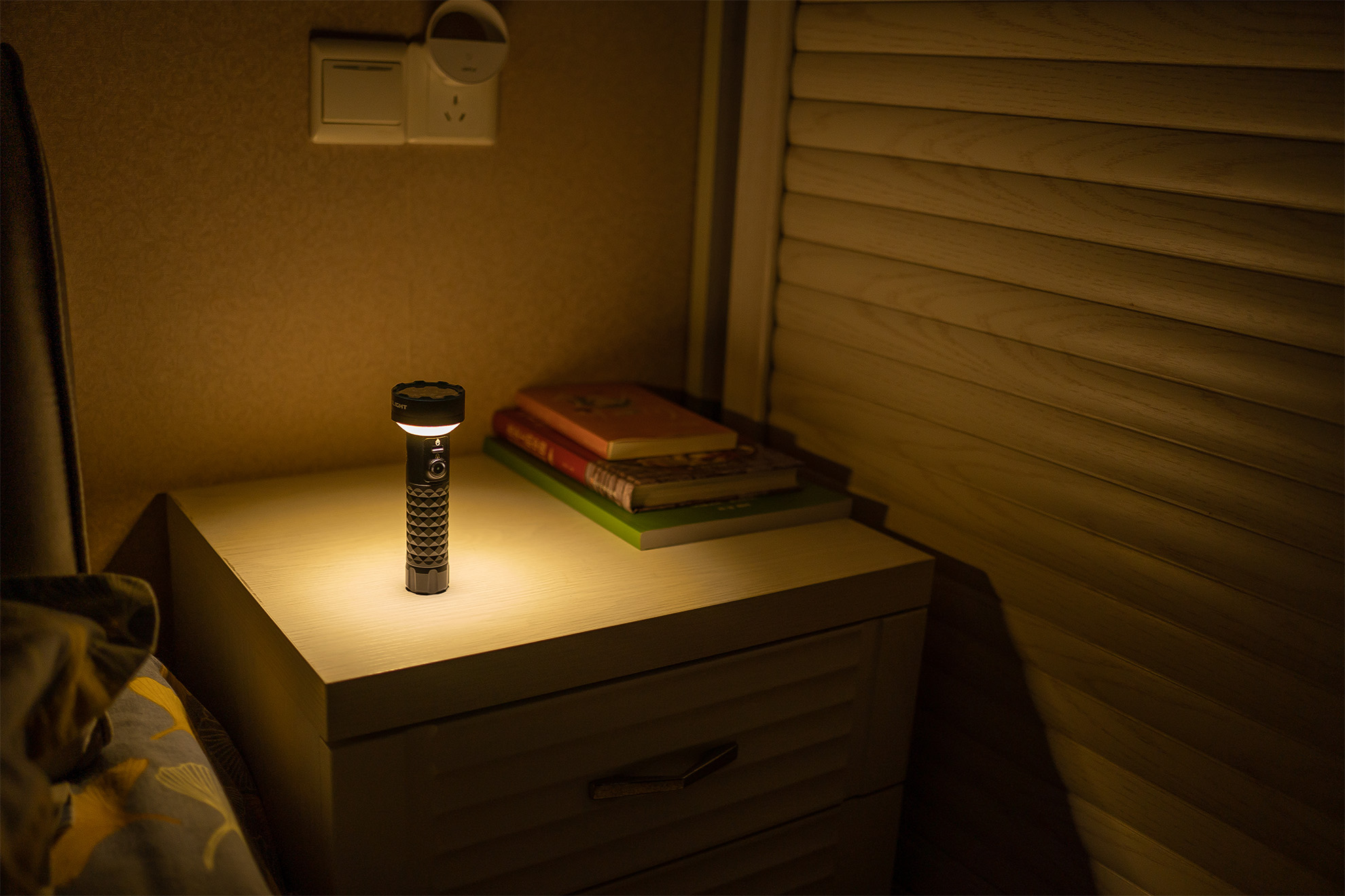 Beleuchtete Taschenlampe auf Nachttisch, spendet warmes Licht im Schlafzimmer neben Büchern. Ideal als Nachtlicht.