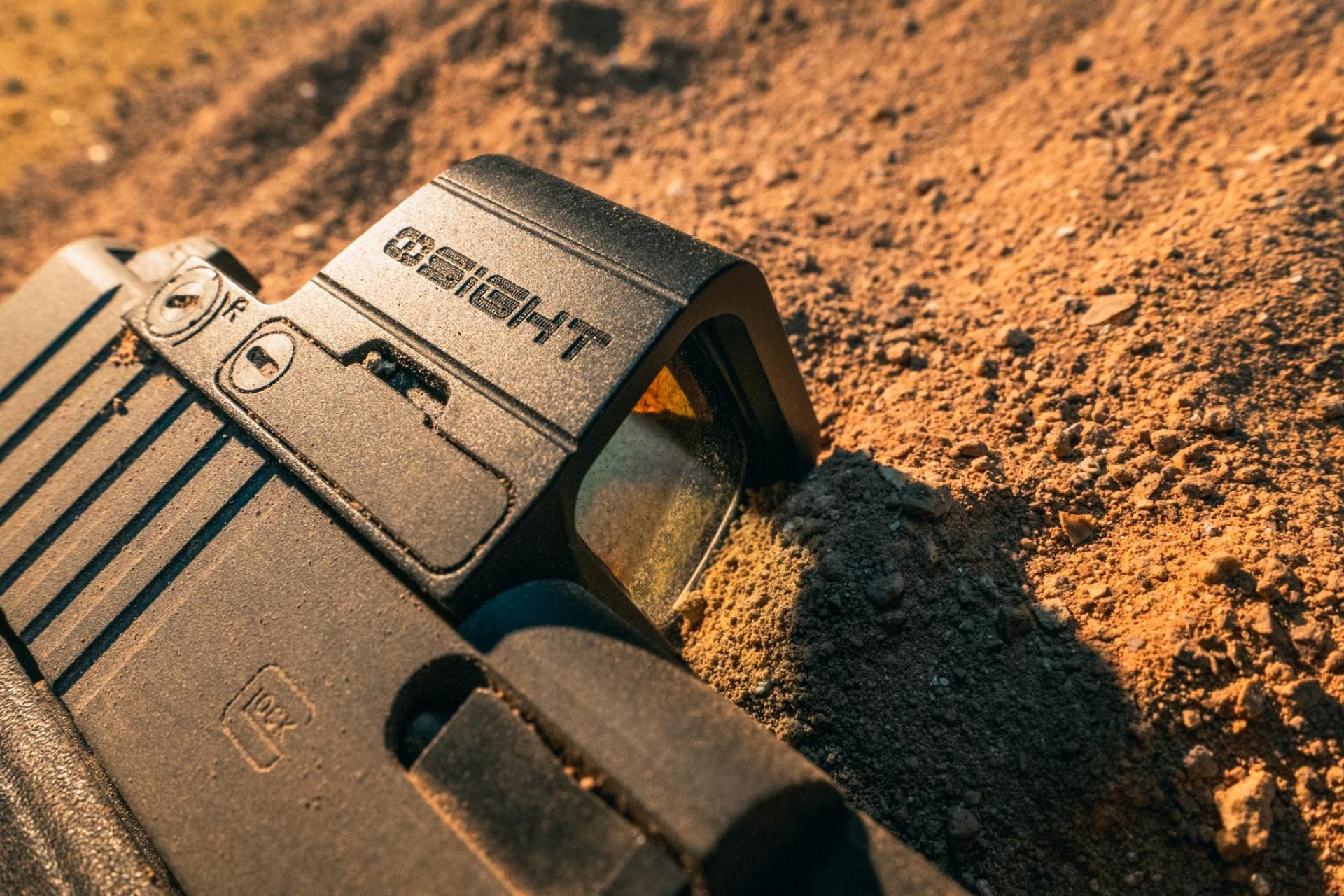 Pistolet Glock avec optique point rouge OSIGHT sur le sable. Optique tactique pour arme à feu, tir en extérieur.