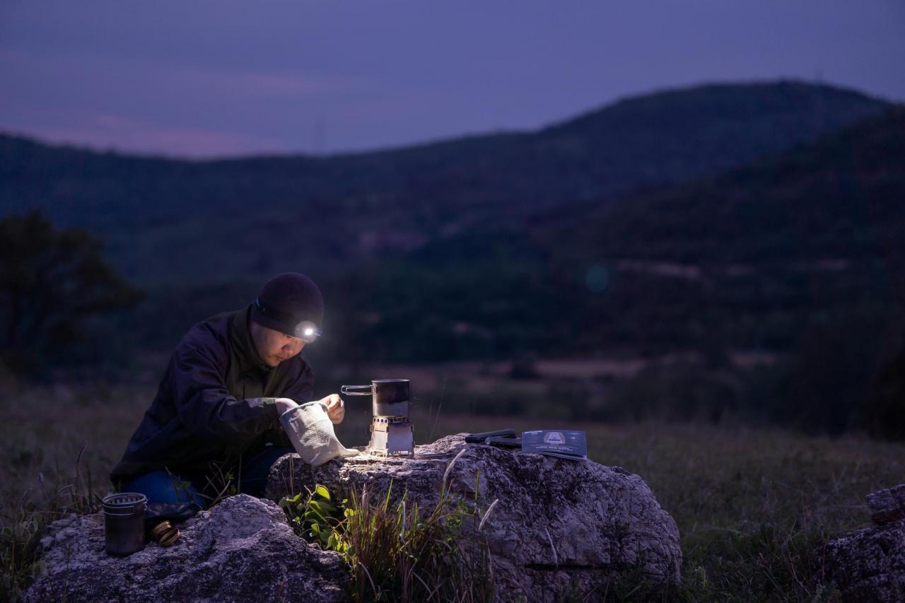 Solo camper using a bright LED headlamp for outdoor cooking at twilight