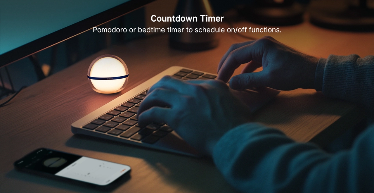 A person typing on a keyboard at night next to a spherical warm LED night light used as a Pomodoro countdown timer or bedtime scheduler.