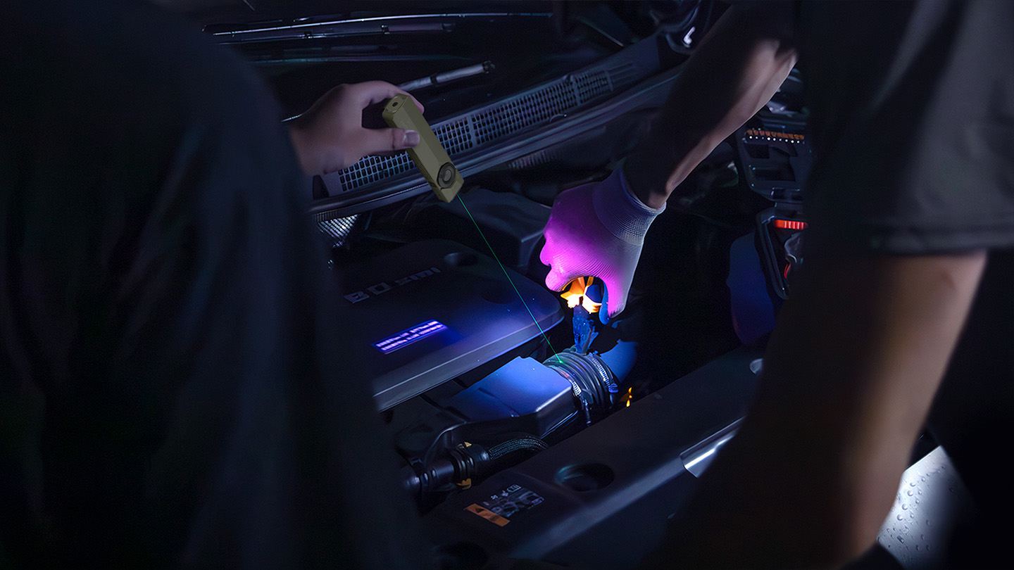 Car mechanics using a green laser pointer and UV inspection light to identify engine issues