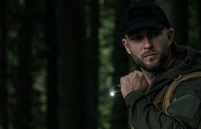 Using a compact high-lumen flashlight in a dark forest for outdoor survival and camping.