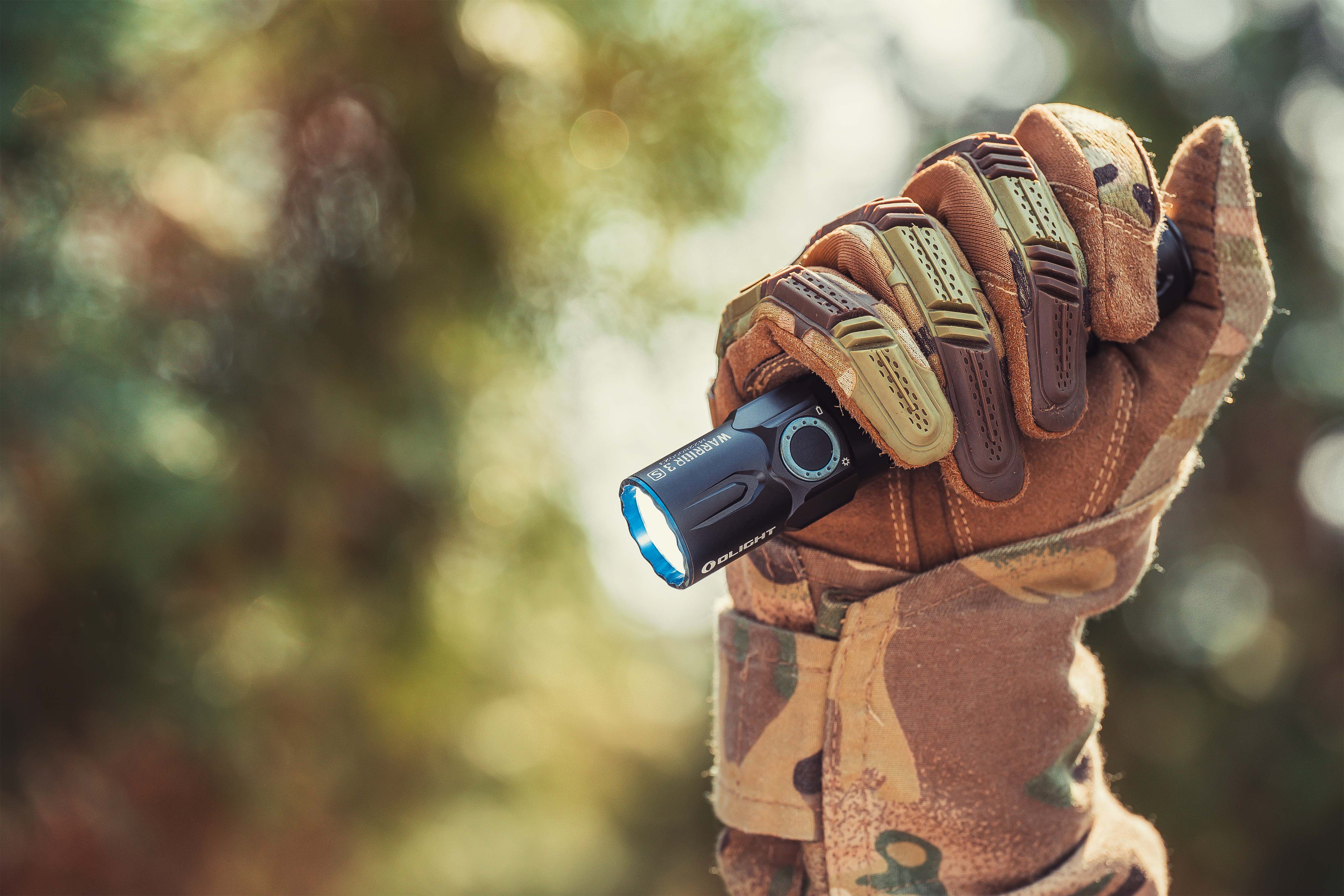 タクティカルグローブを装着した手がOlight Warrior 3Sフラッシュライトを握り、強力な光を放つ