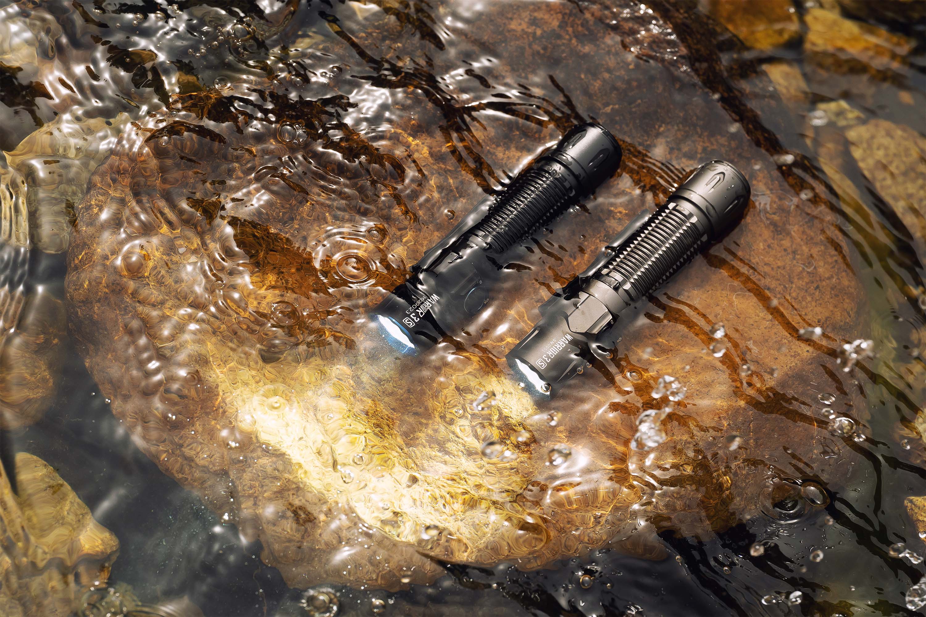 水中の岩に置かれた2つのWarrior 3Sモデル防水懐中電灯。光を放つ高性能アウトドアライト。