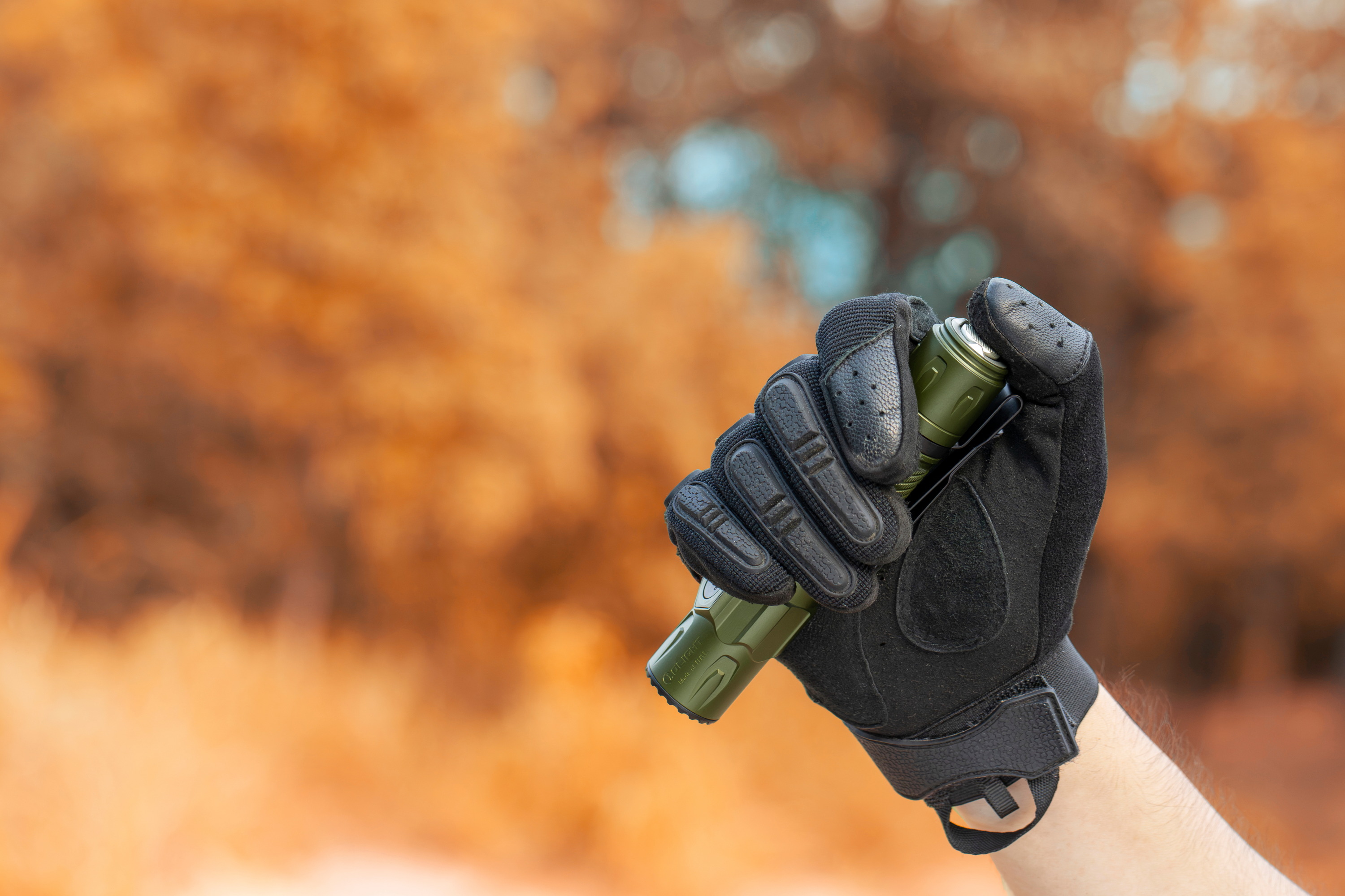 Main gant&eacute;e tenant une lampe torche tactique Olight verte en ext&eacute;rieur en automne