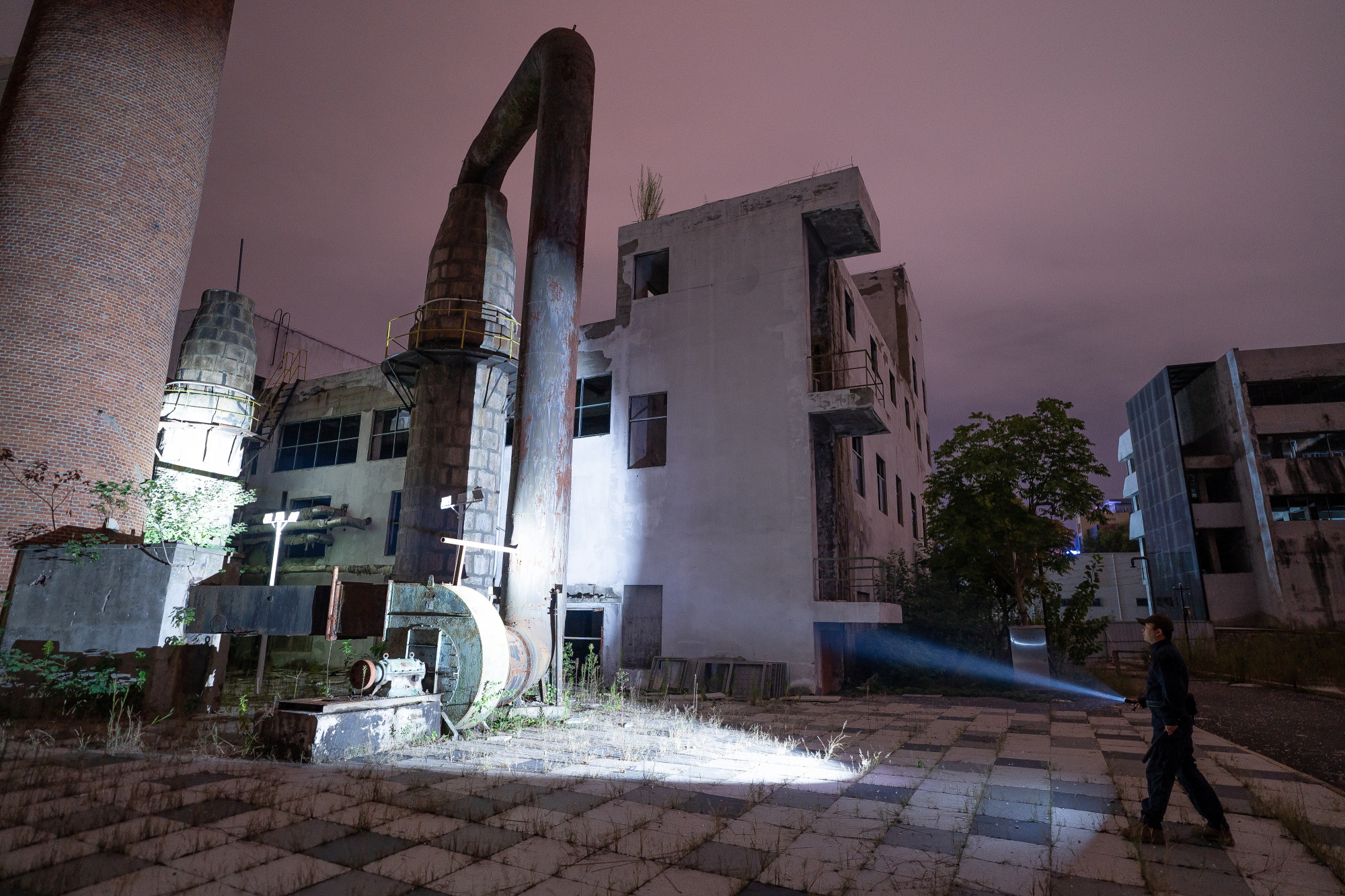 夜の廃墟工場を探検する男性が懐中電灯で道を照らす